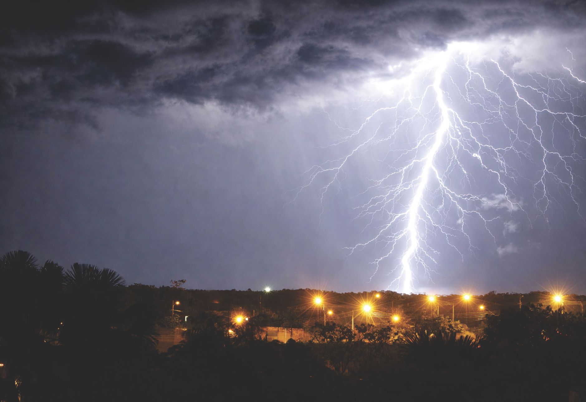 Piorun rozświetlający nocne niebo nad miastem podczas burzy